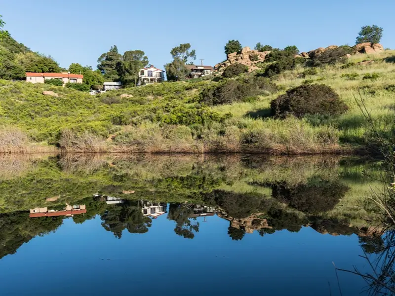 Hillside homes reflected in a calm pond.