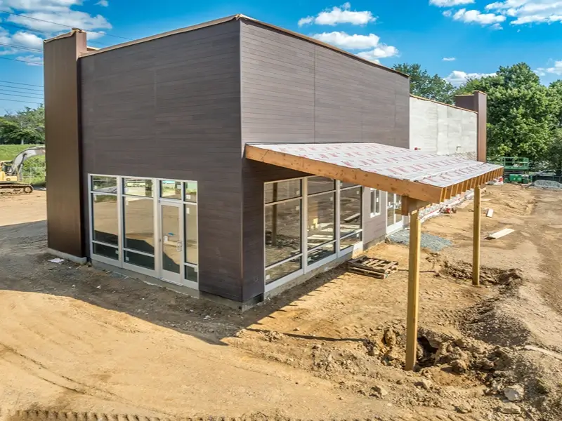 Modern building under construction with large windows and a covered entrance.