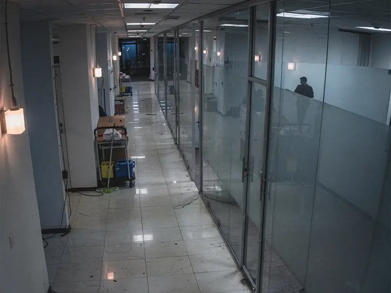 Empty office hallway with glass-walled rooms and cleaning supplies.