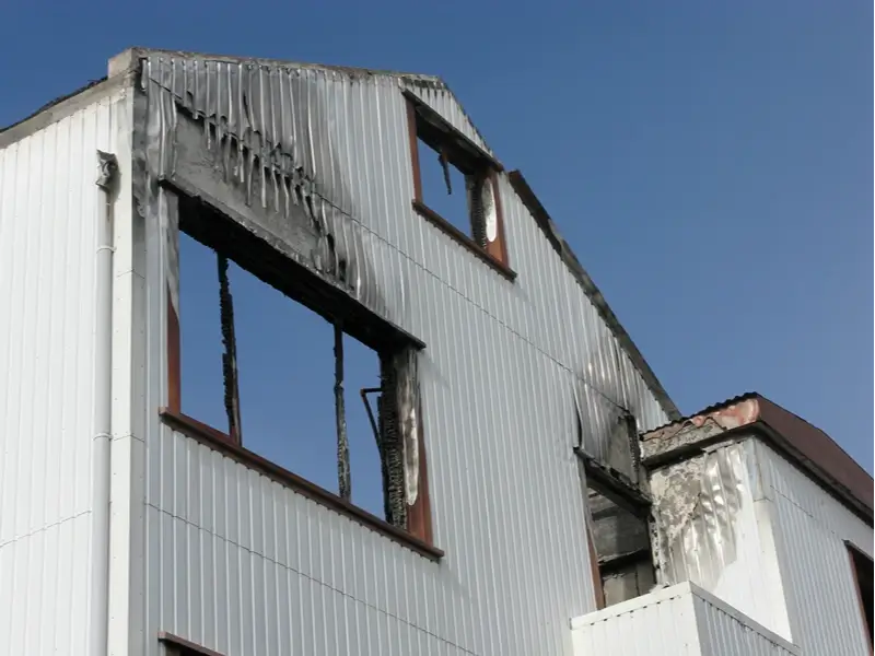 Burned corrugated metal building with charred window openings.