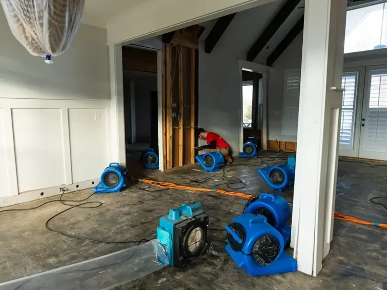 Worker using fans to dry a flooded room under renovation.