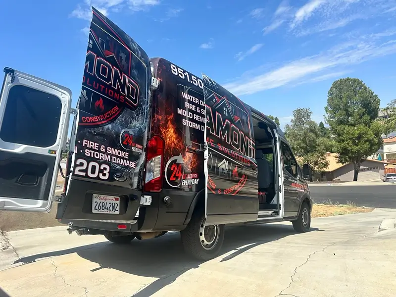 Wrapped service van with open rear doors parked in a driveway.