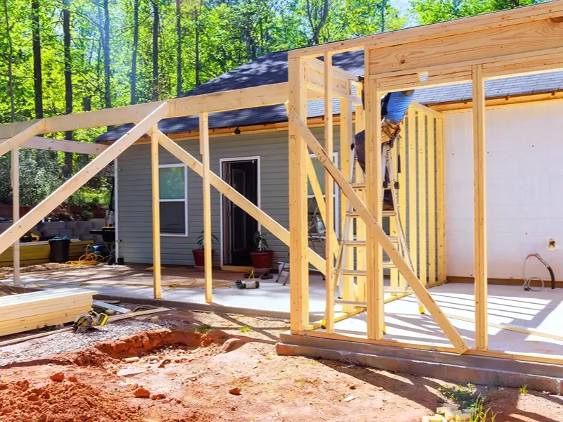 House under construction with wooden framing and a worker on a ladder.